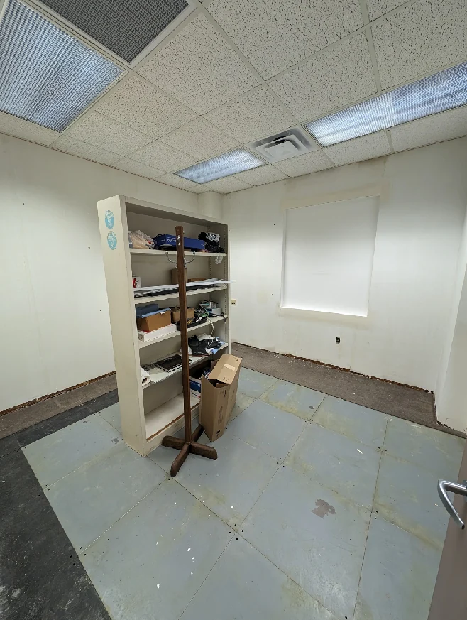 Sitterson 135 before its renovation: an empty room with a bookcase, old floor finishes and blank walls.