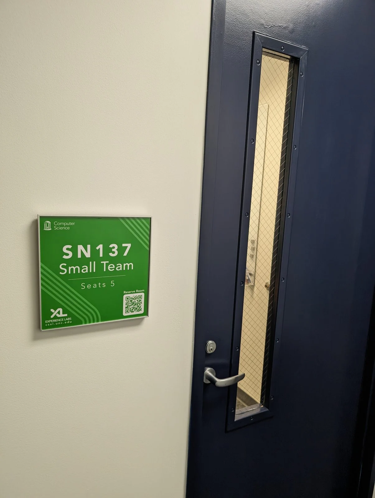 Glossy green SN137 Small Team Seats 5 plaque mounted beside a navy door
