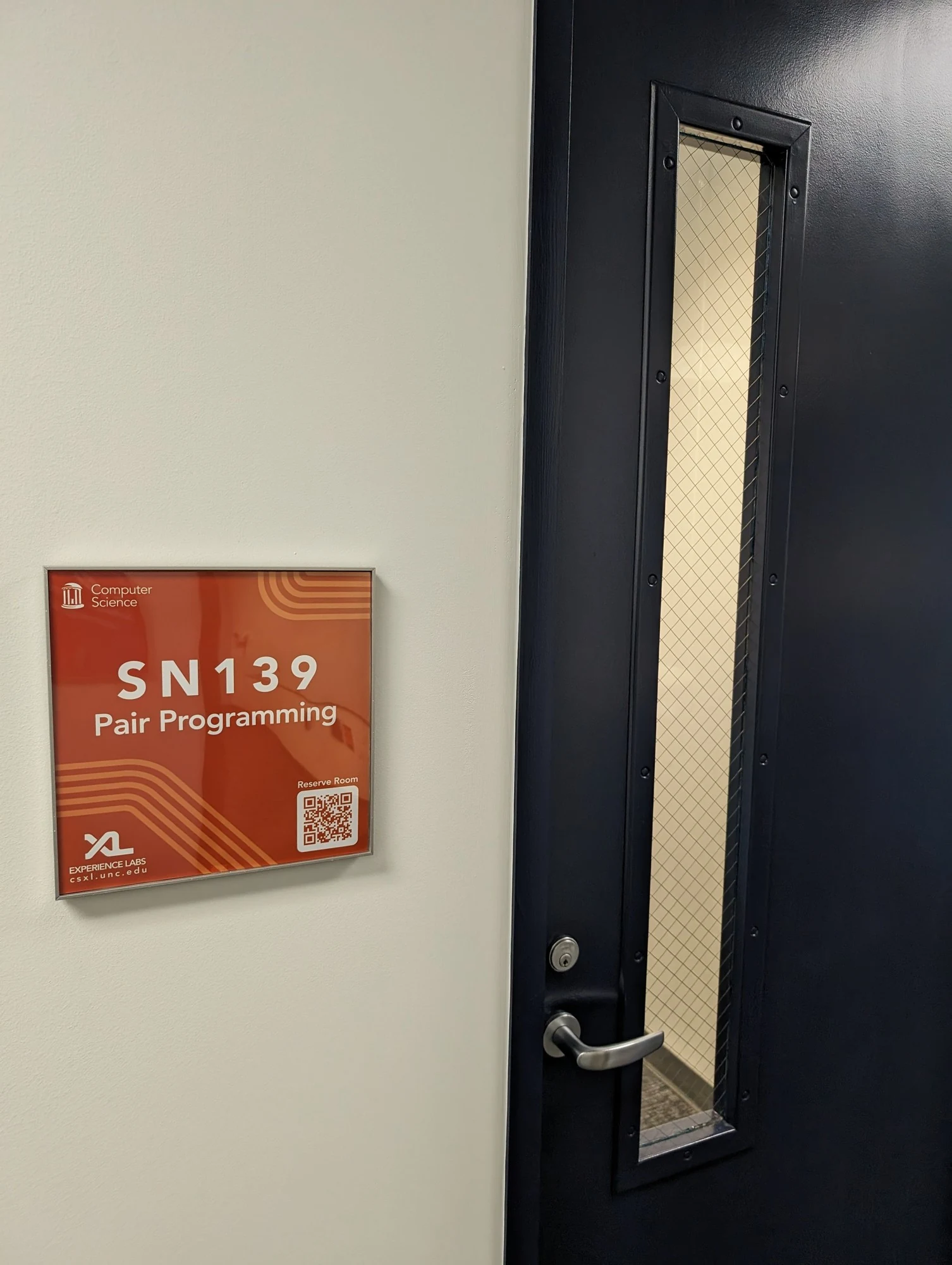 Glossy orange SN139 Pair Programming plaque mounted beside a navy door