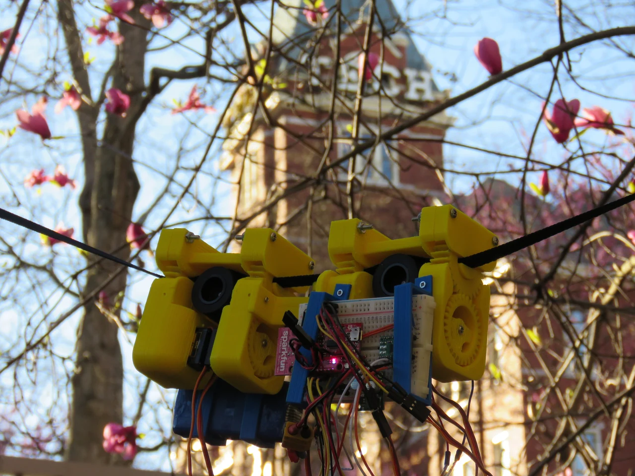 An early yellow SlothBot prototype with exposed electronics suspended from a cable